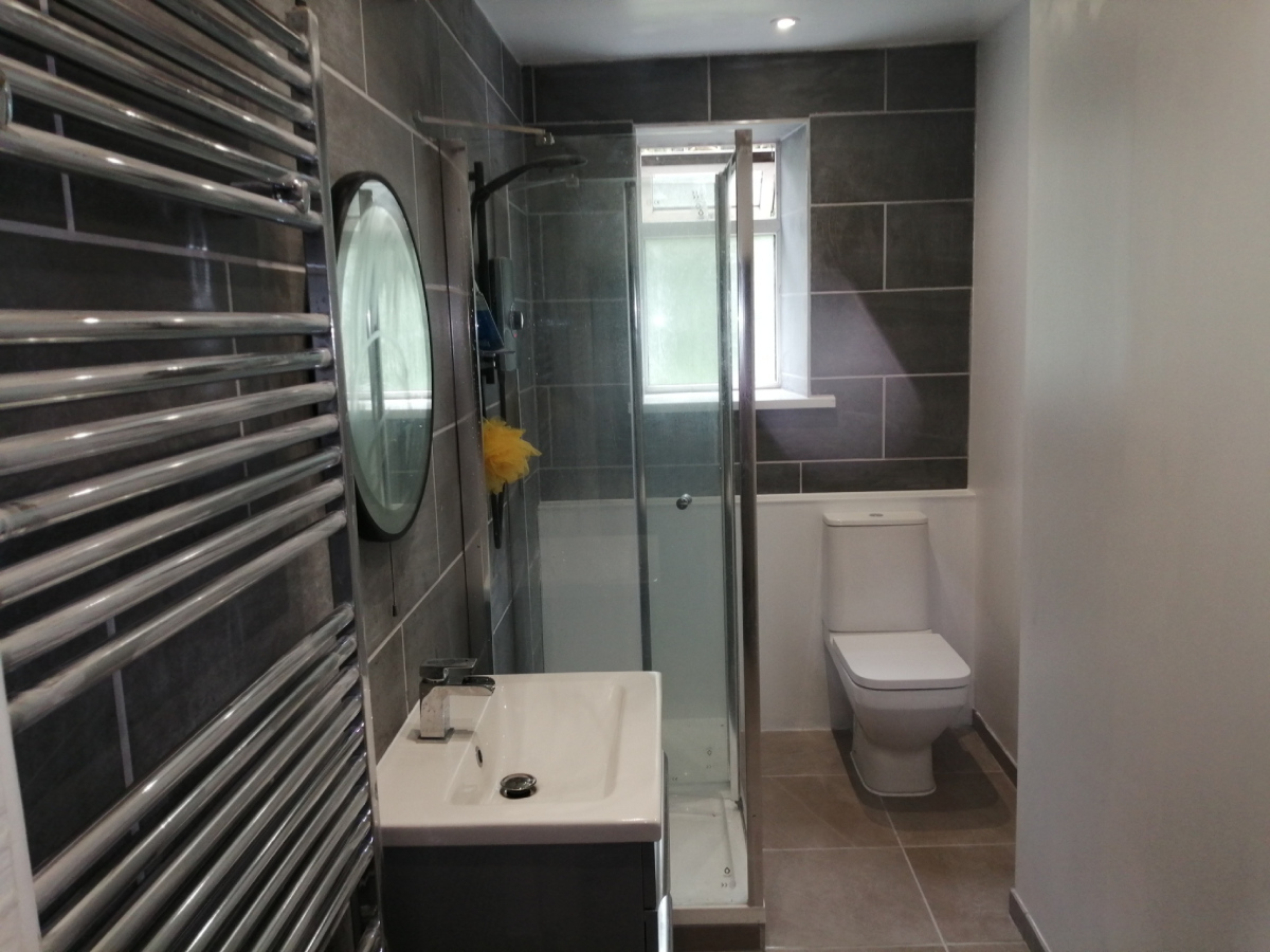 Finished small bathroom with two tiled walls, single shower base, sink unit and floor tiles