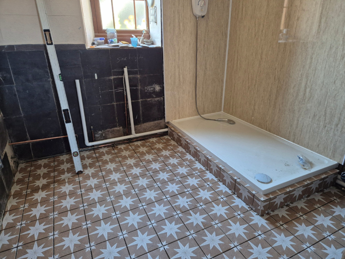 Tiling finished with panelling on shower walls and pipework ready to connect to sink unit and washing machine